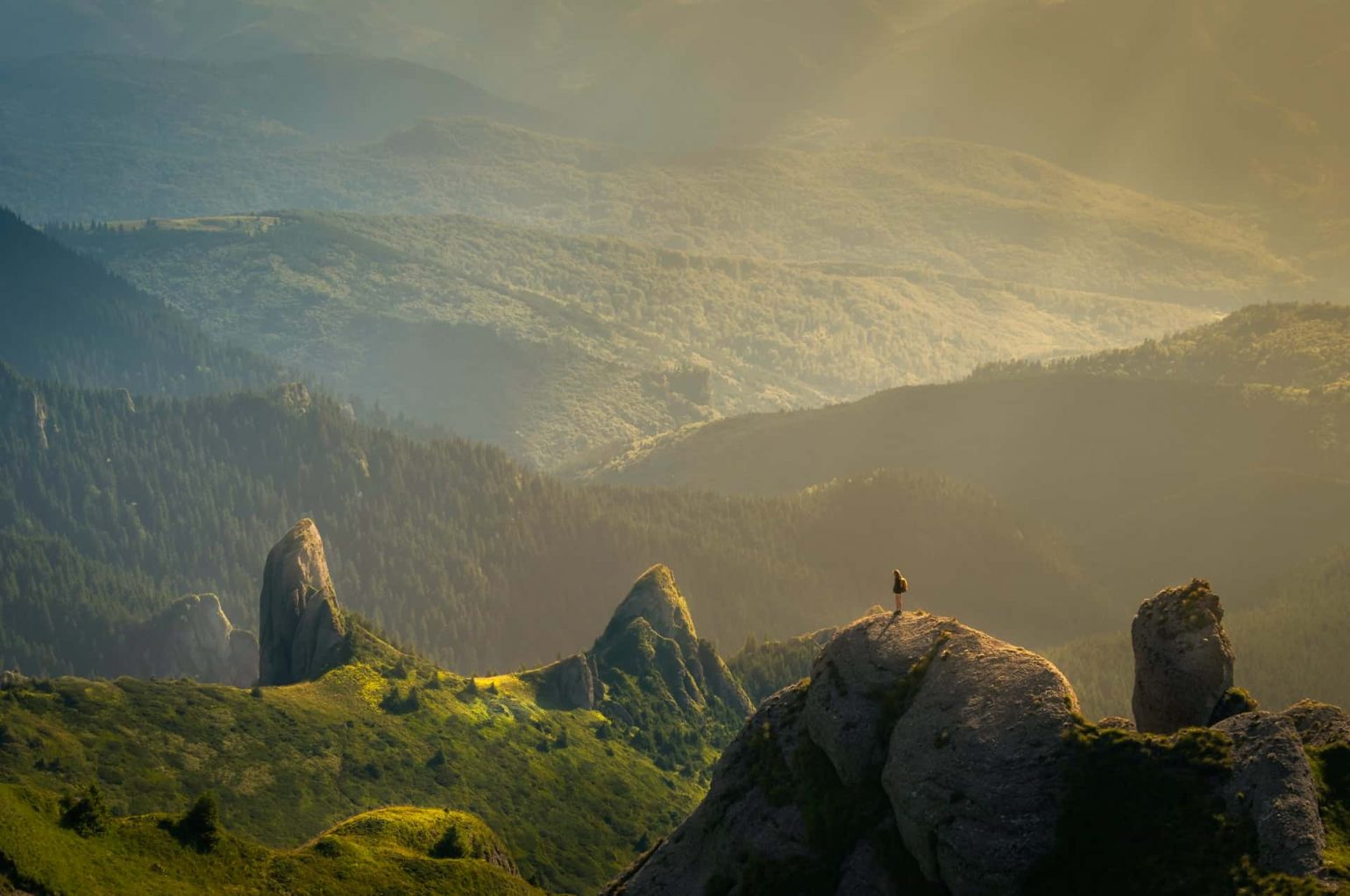 An image of a singluar person in the distance on a outcropping in a vast mountain wilderness