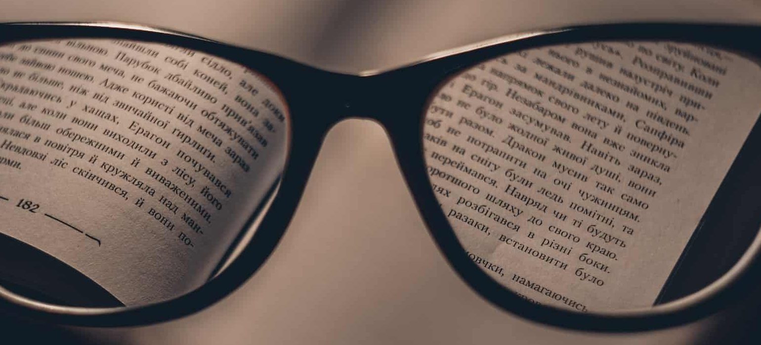 glasses being held in front of a heavy book allowing for the text to be seen more clearly