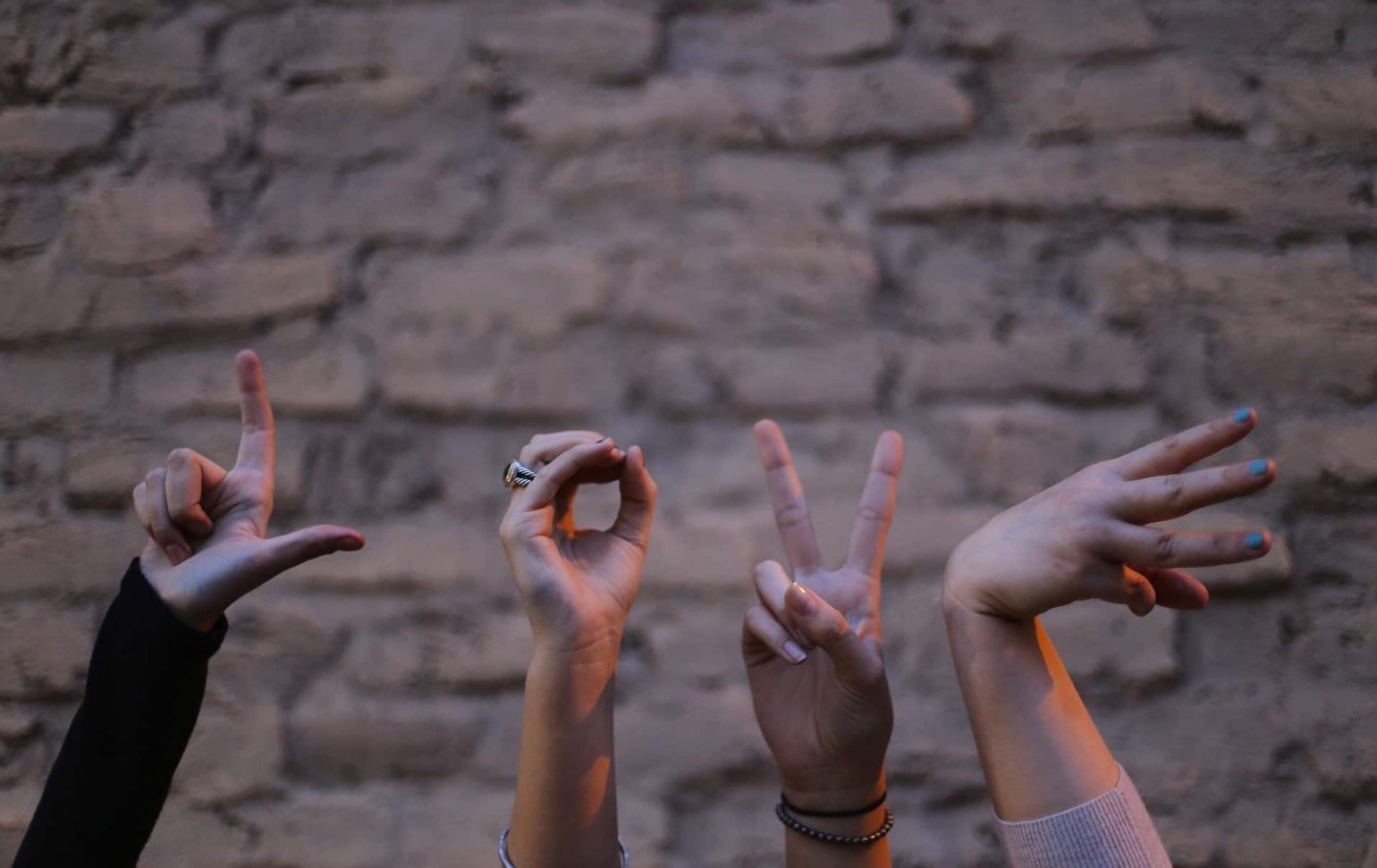 images of 4 people hands up in the arm in front of a brick wall making the letter L, O, V, E