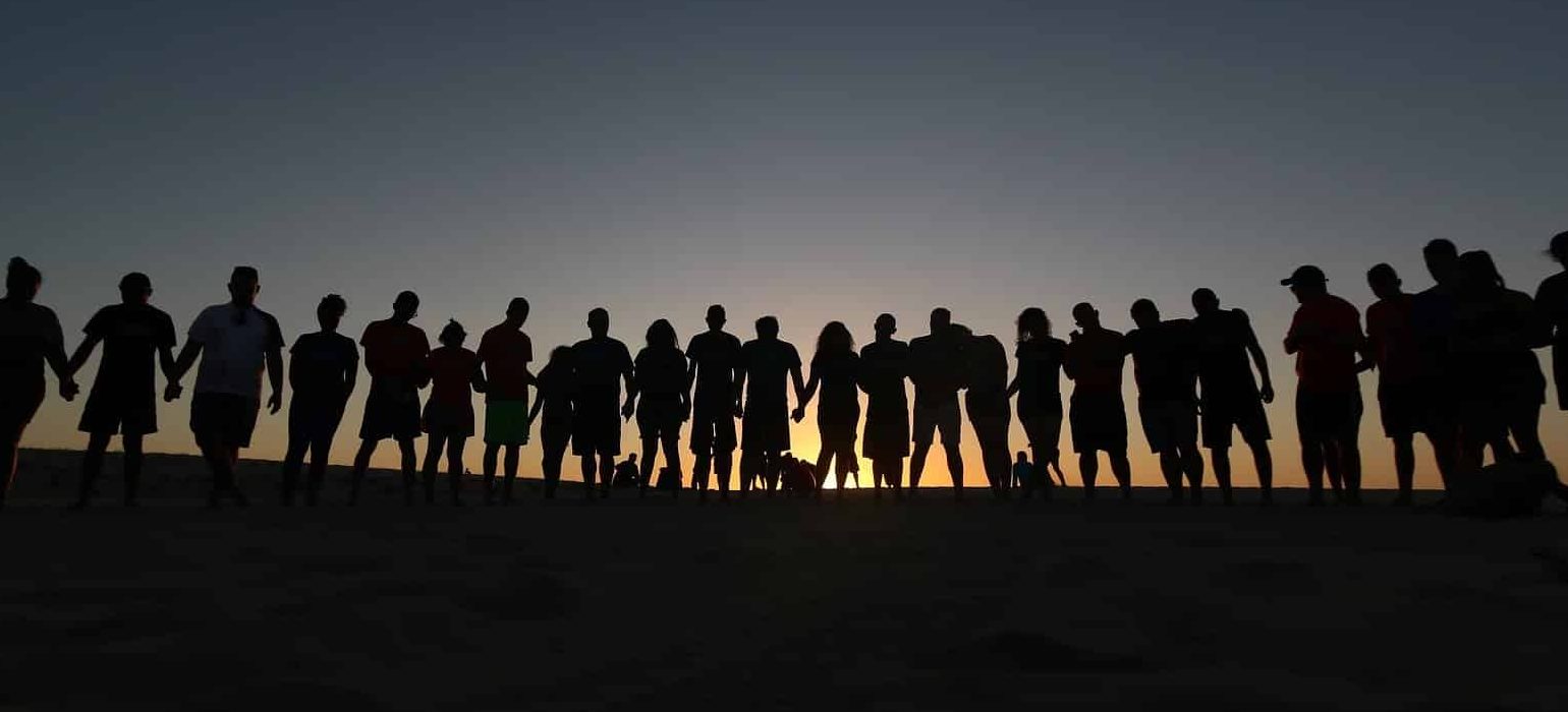 A line of people standing shoulder to shoulder and holding hands during a sunset