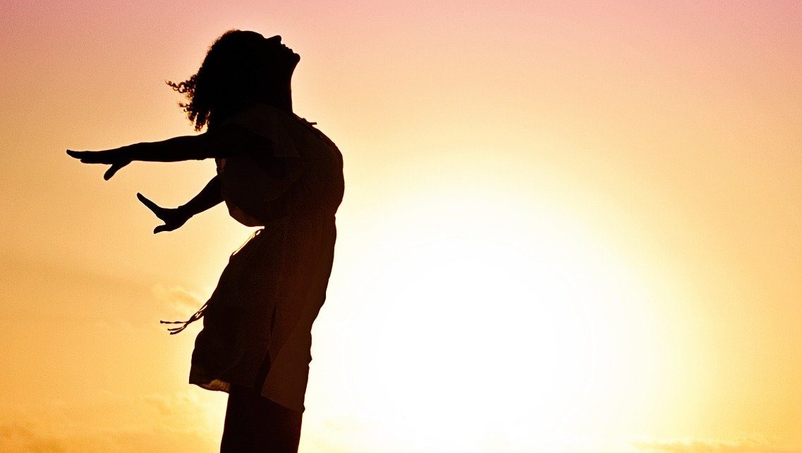 silhouette of a woman on the beach standing tall with her arm spread wide