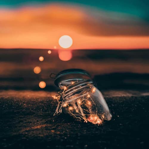 Photo of a glass jar half buried in the sand with little light bulbs illuminated in it